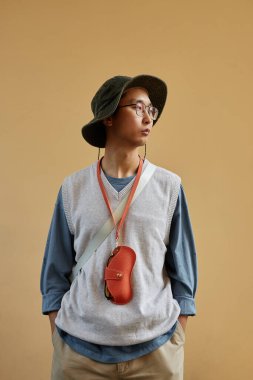 Asyalı bir adamın dikey bel portresi bol günlük kıyafetler giymiş ve arka planda aksesuarlar takmış.