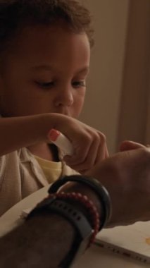 Dikey yan bakış açısı, genç Afro-Amerikan babasının modern evdeki küçük oğluyla birlikte masada işaretlerle resim yaptığı görüntüler.