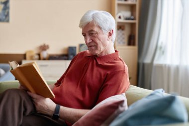 Beyaz saçlı son sınıf öğrencisinin kanepede oturup, fotokopi çekilen evde rahatlama gününün tadını çıkarırken çekilmiş bir portresi.