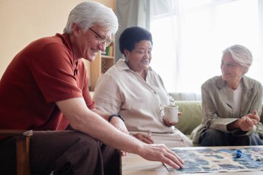 Arkadaşlarıyla oyun oynayan gülümseyen beyaz saçlı son sınıf öğrencisinin yan görünüm portresi.