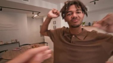 Kahverengi polo tişörtlü, geniş bir dairede sevgilisiyle enerjik bir şekilde dans eden çift ırklı adamın görüntüsü.