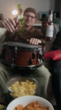 Çok ırklı erkek arkadaş ve spor fanatiklerinden oluşan dikey zum yavaş çekim. Hafta sonu TV 'de futbol maçı izlemek için kanepede toplanırken bira şişeleriyle kadeh kaldırıyorlar.