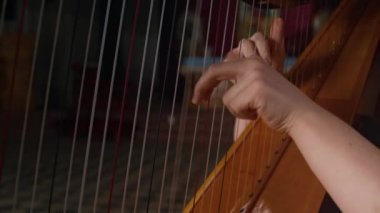 Açık kolları olan genç bir kadının, ahşap arp üzerinde kendine güvenen telleri koparıp arka planda bulanık katolik simgelerle solo performans sergilediği sahneler.