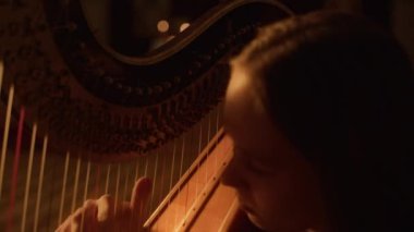 Yakın plan çekimde, beyaz tenli bir arpçı, arka planda bulanık mumların loş ışıklarıyla nazikçe meditasyon yaparken görülüyor.