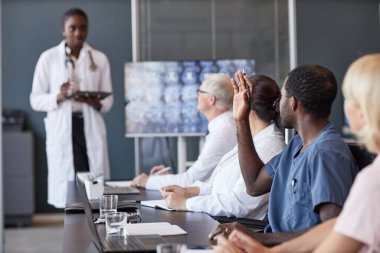 Afrika kökenli Amerikalı erkek klinisyenlerin el kaldırarak meslektaşlarına konferans masasında otururken grup seminerinde sunum üstüne soru sormaları ve uzayı kopyalamaları.