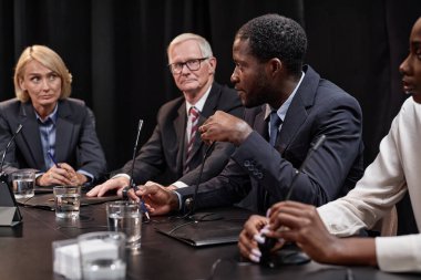 Kenar görüşlü Afrikalı Amerikalı politikacının mikrofona konuştuğu kadın meslektaşı ile toplantı masasında diğer yetkililerle otururken inisiyatifi tartıştığı, alanı kopyaladığı