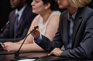 Takım elbiseli kadın politikacının basın toplantısı sırasında masada diğer yetkililerle otururken mikrofonu ayarlarken görüntüsü kesildi.