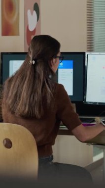 Yaratıcı ofisteki çift monitörde çalışan kadın profesyonelin dikey orta görünüm görüntüsü