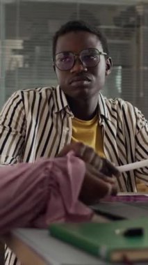 Genç siyahi adamın dikey beliyle beyin fırtınası toplantısında yaratıcı fikirleri tartışması modern ofiste üzerinde not defterleri ve kırtasiyelerle masada oturması.