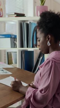 Modern ofiste birlikte çalışan ve tasarım taslaklarını gözden geçiren etnik çeşitliliğe sahip iki genç bayan meslektaşın dikey çizimi. Biri oturmuş, çizimleri analiz ederken, diğeri de yakınlardaki fikirlere katkıda bulunuyor.