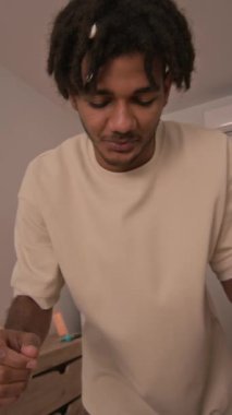 Babalık iznindeki genç melez adamın dikey görüntüsü. Çocuğunu sıcak çocuk odasında kaşıkla besliyor.