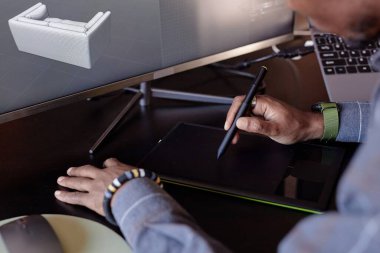 Bilgisayar ekranında üç boyutlu mobilya modelini tasarlamak için dijital tablet ve stil kullanan kişi, çalışma alanındaki el hareketleri ve teknolojiye odaklanıyor