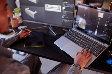 Tasarımcı, modern yaratıcı stüdyoda grafik tablet ve çoklu görev kullanırken dizüstü bilgisayarda ayrıntılı iç modeller oluşturmaya odaklanıyor.