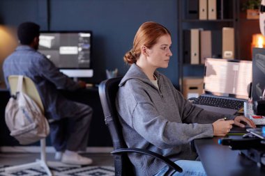 Modern ofis ortamında çalışan iki profesyonel, bilgisayar ekranlarına odaklanıyor, görevleri verimli bir şekilde tamamlıyor ve iyi ışıklandırılmış bir alanda profesyonel bir atmosferi koruyorlar.