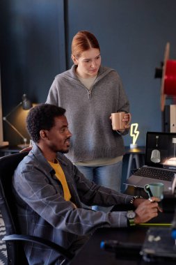 Multiracial colleagues collaborating on project in cozy office space with modern equipment, engaging in focused discussion while reviewing digital content on laptop screen clipart