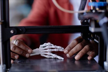 Yakından bakıldığında, insan eli iskelet modelinin karmaşık bir şekilde üç boyutlu baskısını gösteren bir kişi görülüyor. Hassasiyet ve teknoloji üzerine ayrıntılı odaklanma