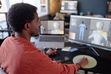 Modern ofis masasında detaylı 3D animasyon projesi üzerinde çalışan bir adam, çift monitörlere, dizüstü bilgisayara ve diğer araçlara odaklanmış durumda.