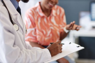 Afro-Amerikalı bir doktorun panoya notlar yazıp belirtileri bulanık arkaplanla açıklarken yan görüntüsü.