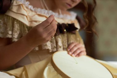 Side view detail shot of young lady guiding thread through fabric doing intricate embroidery in vintage setting, copy space clipart