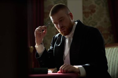 Resmi giyinmiş genç bir beyefendinin romantik portresi. Sofraya hafif ışıklandırmayla mektup yazarken, boşluğu kopyalayarak.