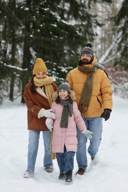 Vertical full length portrait of happy young family walking together in winter forest with daughter smiling cheerfully enjoying holiday vacation clipart