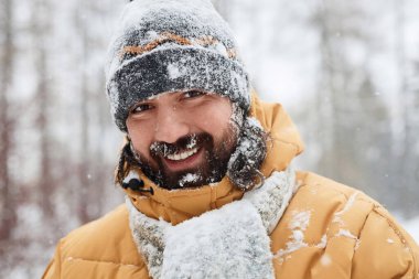 Sakallı yetişkin bir adamın portresi. Karla kaplı kameraya gülümsüyor. Kış ormanında gerçek duygularla.