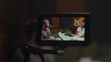 Genç beyaz tenli radyo sunucusuyla podcast çekiminden sahne arkası. Genç bayan Afrikalı Amerikalı konuğu mikrofonla modern yayın stüdyosunun rahat ortamında konuşuyor.