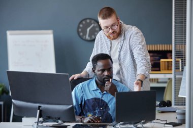 İki meslektaş bir proje üzerinde çalışıyor. Sahnede bilgisayarlar, bir beyaz tahta ve odaklanmış etkileşimli ofis malzemeleri yer alıyor.