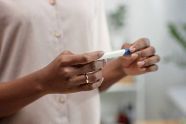 Elinde hamilelik testi olan Afrikalı Amerikalı kadının parmağındaki altın yüzüğe yaklaş. Banyoda, fotokopi odasında sonuçları bekliyor.