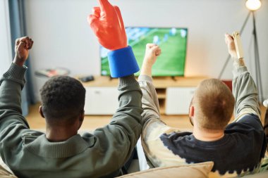 Heyecanlı spor taraftarlarının TV 'de maç izlerken kanepede oturup zaferi kutlayan ellerini kaldırması, kopyalama alanı.