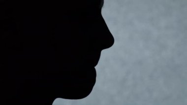 Yandan yakından bakınca, tanımlanamayan koyu siyah erkek siluetinin dudağını gri renkte arka planda ısırdığını görüyoruz.