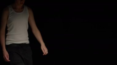 Göğsünde beyaz fanilalı bir adam portresi var. Lekeli sandalyeye oturmuş kameraya ciddi ciddi bakıyor. Derin siyah stüdyo arka planına bakıyor.