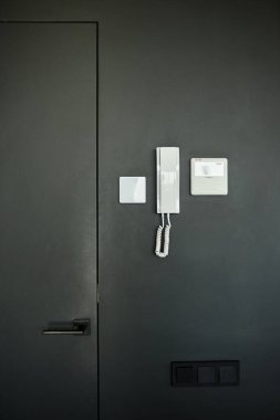 Elektronik panelin dikey görüntüsü ve mikrofonlu cep telefonu. Minimalist apartmanın içindeki siyah duvarda asılı konuklarla konuşmak için.