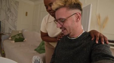 Genç ve mutlu beyaz bir adam ve genç siyah bir kadın kameraya konuşuyor ve tatlı Fransız buldoguyla rahat bir oturma odasında video kaydediyor.