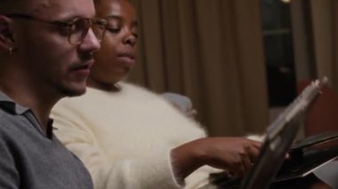 Kafkasyalı genç bir adam ve siyah bir kadının rahat bir şekilde kanepede oturup plakları seçerken ve hangi albümü dinleyeceklerini tartışırken yan görüntüsü.