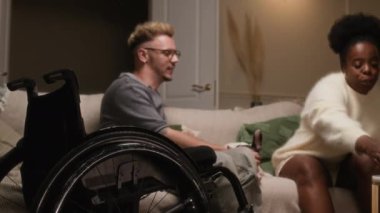 Orta boy beyaz adam ve genç Afrikalı Amerikalı kadın rahat koltukta köpekle oturuyor, sohbet ediyor, şarap içiyor, tekerlekli sandalyede ön planda akşam yemeğinin tadını çıkarıyor.