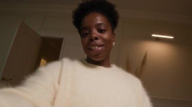 Genç, sakin, rahat, rahat, rahat kazaklı bir kadın kameraya konuşuyor ve akşamları evdeki rahat oturma odasında video kaydediyor.