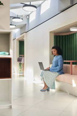 Dizüstü bilgisayarda yazan, modern çalışma alanının oturma odasındaki koltuklarda çalışan genç bir kadının dikey çekimi, kopyalama alanı.