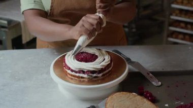 Önlüklü, tanınmayan kadın fırıncının yavaş çekimleri ahududu kekinin üzerine tatlı krema serpiştiriyor.