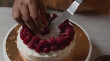 Tepeden tırnağa, tanınmayan pasta şefinin taze ahududu ve kirazla kremalı pastayı süslediği yakın çekim.