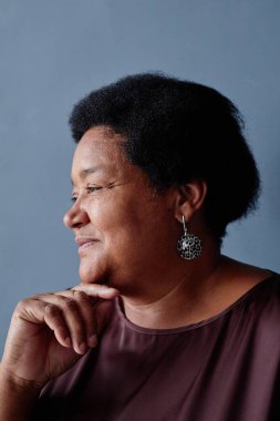 Stüdyoda mavi arka plana bakıp gülümseyen yaşlı Afro-Amerikan kadının minimal yan görüntüsü.