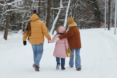 Kızlarının kış ormanlarında karların üzerinde yürüyüp el ele tutuşup uzayı kopyaladığı mutlu aile manzarası.