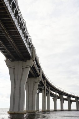 Suyun üzerindeki yüksek sanayi köprüsünün dikey arkaplan görüntüsü, soluk beyaz gökyüzü, insan yok