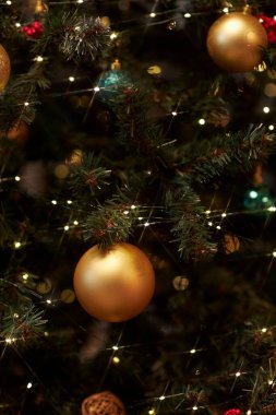 Süslü Noel ağacının parlak ışıklarıyla süslenmiş altın baloncuklarının dikey yakın çekimi alanı kopyalar