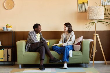 Neşeli Afrikalı Amerikalı bir adam kahve molası sırasında genç bayan meslektaşıyla sohbet ederken modern rahat ofiste rahat bir koltukta oturup, fotokopi çekerken iş konularını tartışıyor.