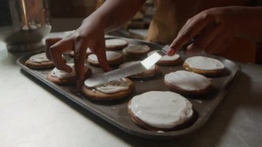 Tanınmayan hamur işi şefinin lezzetli kurabiyelerin üzerine tatlı krema ve paslanmaz çelikten spatulayla sürmesi.