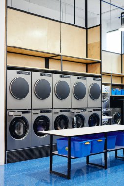 Çift sıra profesyonel çamaşır makineleri ve çamaşır kurutma makinelerinin katlanan masaya yuva yaptığı modern self servis çamaşırları.
