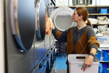 Çağdaş self servis çamaşır odasında çamaşır makinesini çamaşır makinesiyle dolduran kadın müşterinin yan görüntüsü