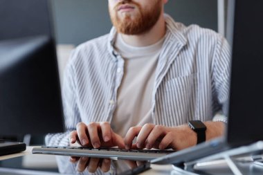 Çağdaş ofis ortamında çift monitörlerde kodlama projelerine odaklanmış erkek programcı, çizgili gömlek giyiyor ve eldeki göreve özen gösteriyor