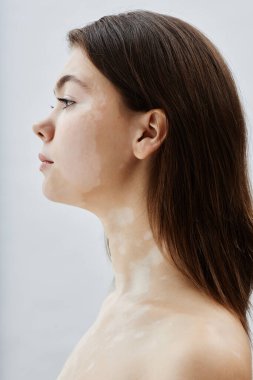 Stüdyoda beyaz arka plana karşı poz veren rahat ve genç bir kadının dikey profil çekimi beyaz beneklerin doğal güzelliğini kucaklıyor.